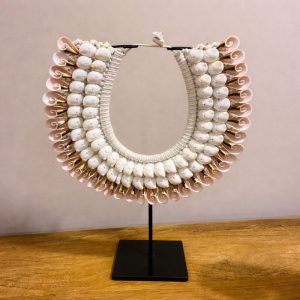 Επιτραπέζιο χειροποίητο διακοσμητικό κολιέ από φυσικά κοχύλια σε αποχρώσεις του λευκού και του απαλού ροζ, τοποθετημένο σε κομψή μαύρη μεταλλική βάση. Ένα ξεχωριστό statement piece που συνδυάζει την αυθεντικότητα της φύσης με την εξωτική αισθητική. Ο πλούσιος όγκος των κοχυλιών και η περίτεχνη πλέξη δημιουργούν ένα εντυπωσιακό αποτέλεσμα που τραβά αμέσως το βλέμμα. Ιδανικό για boho, ethnic, island ή coastal διακόσμηση, δίνει χαρακτήρα και ιδιαίτερο στυλ σε σαλόνι, είσοδο, κονσόλα ή επαγγελματικό χώρο. Κάθε κομμάτι είναι χειροποίητο και μοναδικό, γεγονός που το καθιστά πραγματικό διακοσμητικό κόσμημα για τον χώρο.