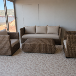 Χειροποίητο σετ σαλονιού από φυσικό rattan με τριθέσιο καναπέ, δύο πολυθρόνες, τραπεζάκι και εκρού μαξιλάρια, ιδανικό για στεγασμένους εξωτερικούς και εσωτερικούς χώρους.
